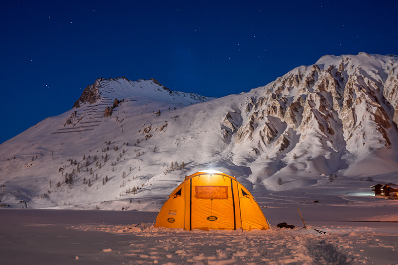 Tente d’expédition éclairée au pied de montagnes enneigées